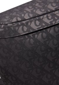 Tejido negro texturizado con un patrón abstracto repetido. Forma rectangular con detalles cosidos a lo largo de los bordes. Acabado suave.