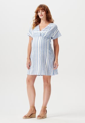 Robe de maternité à rayures bleu clair et blanches avec un décolleté en V, des manches courtes et un design croisé. Portée avec des sandales à talons compensés couleur beige.