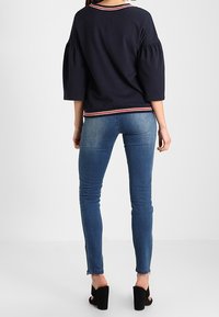 Pullover blu navy con maniche a sbuffo, scollo a coste e orlo a righe. Abbinato a jeans blu aderenti e sandali neri con tacco alto.