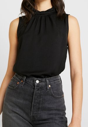 Ærmeløs sort top med samlet halsudskæring, båret indstoppet i højtaljede, falmede sorte jeans med forreste knaplukning og lommer.