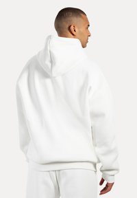 Haut à capuche blanc avec une coupe décontractée, capuche à l'arrière, poignets et taille côtelés ; fabriqué en tissu doux et texturé.