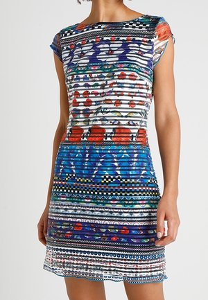Femme portant une robe ajustée à manches courtes avec des rayures horizontales multicolores et des motifs géométriques et floraux.