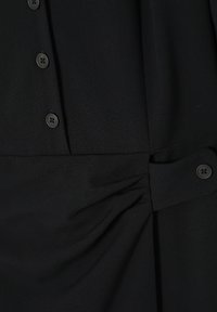 Schwarze Bluse mit Knopfverschluss, glatter Textur und gerafften Details an der Taille für einen maßgeschneiderten Look.