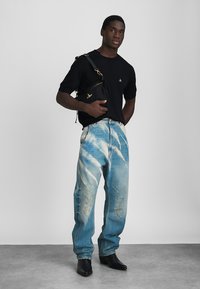 Svart kortermet skjorte, lyseblå slitte jeans med batikkmønster og svarte spisse støvler, kombinert med en svart skulderveske.