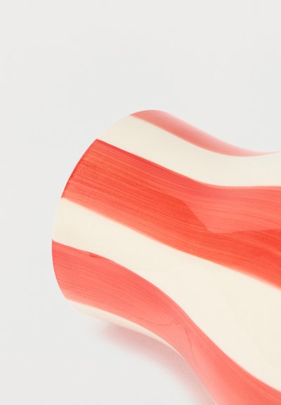 Καμπυλωμένο κεραμικό αντικείμενο με εναλλασσόμενες φαρδιές κόκκινες και λευκές κάθετες ρίγες πάνω σε ανοιχτό φόντο.