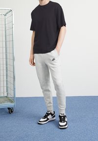 Svart bomull t-shirt, grå sweatpants med Nike-logga och svartvitt träningsskor. Avslappnad outfit mot en dämpad bakgrund.