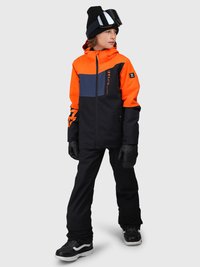 Barn som har på seg en oransje, svart og marineblå skijakke med sorte snøbukser, sorte hansker, svart lue og skibriller, står mot en grå bakgrunn.