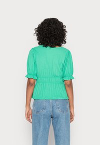Blusa texturada verde com mangas curtas bufantes, cintura elástica e decote redondo, combinada com jeans azuis de cintura alta.