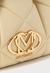 Μπεζ καπιτονέ γυναικείο τσαντάκι με χρυσό λογότυπο Love Moschino με συνυφασμένα γράμματα, λεία υφή και δομημένο σχέδιο.
