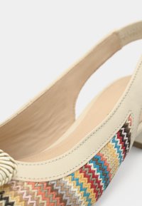 Μπεζ δερμάτινο παπούτσι με ανοιχτή φτέρνα, με πολύχρωμο υφαντό σχέδιο στο πλάι. Ομαλή υφή με λεπτομέρειες κρόσσι στο δάχτυλο.