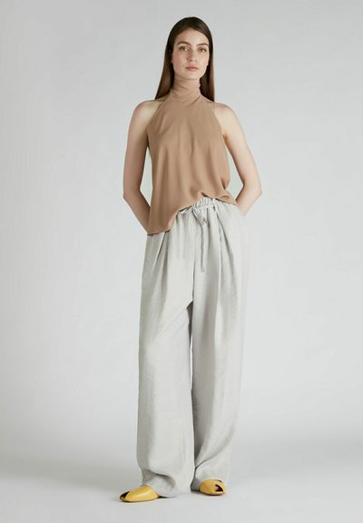 Top halter beige con una texture morbida, abbinato a pantaloni grigi chiari, larghi e con vita regolabile, leggermente drappeggiati, completi di infradito gialle.