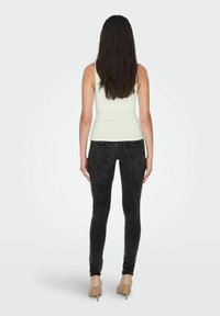 Jeans ajustados negros con textura desgastada, diseño de cintura alta y bolsillos traseros, combinados con una blusa sin mangas clara y tacones nude.
