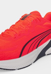 Φωτεινό κόκκινο αθλητικό παπούτσι Puma με μαύρη ρίγα και λευκή σόλα, σε γωνία που δείχνει το πλάι και την κορυφή με κορδόνια και λογότυπο της μάρκας.