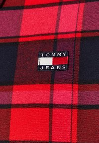 Tessuto a quadri rosso e nero con una texture morbida. Presenta un'etichetta ricamata "TOMMY JEANS" blu e bianca.