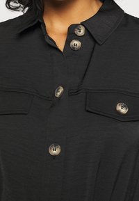Black button-up shirt featuring a collared neckline, two chest pockets, and light-colored buttons with a marbled texture.