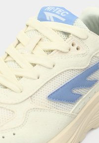 Krēmkrāsas un zilas sporta apavi ar sieta augšdaļu, zamšāda akcentiem, plakaniem šņorēm un teksturētu zolīšu dizainu, lai nodrošinātu saķeri.