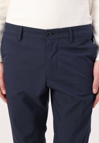 Navy blue trousers with a flat front, single button closure, side pockets, and a textured fabric. Tailored fit with classic design elements.