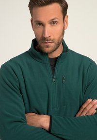 Pullover in pile color teal con colletto con zip, caratterizzato da due zip frontali e una superficie liscia. Maniche lunghe con bordo nero sui polsini.