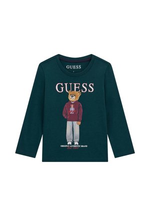 Maglia a maniche lunghe verde scuro con un orsacchiotto che indossa una felpa con cappuccio e jeans, logo "GUESS" sopra e testo "Original Authentic Brand Est. 1981" sotto.