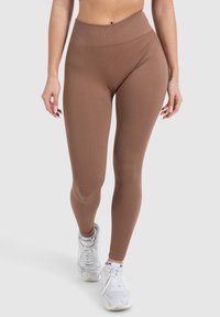 Leggings marroni a coste con vita alta, forma aderente e tessuto elastico, abbinati a sneaker bianche per un look sportivo.