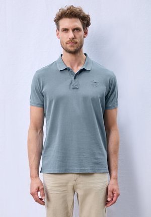 Polo en bleu clair, fabriqué en coton doux, avec un col classique, des manches courtes et un logo subtil sur la poitrine.