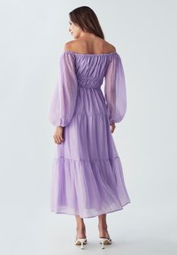 Violetti olkaamatta oleva mekko, jossa on pitkät puffihihat, kootut vyötärö ja kerrostettu hame. Valmistettu kevyestä, teksturoidusta kankaasta.