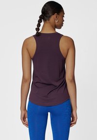 Fioletowy sportowy top na ramiączkach z okrągłym dekoltem i dopasowanym krojem, zestawiony z niebieskimi legginsami w wzory. Gładki materiał i minimalistyczny design.