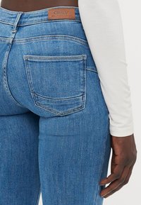 Blå denimjeans med en figurnära design, med en brun läderlogotyp, bakfickor och en mjuk textur.