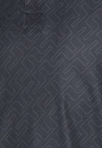 Marinblått tyg med ett upprepande geometriskt mönster, som har en subtil lyster. Sömnadsdetalj nära toppen med en upphöjd kragsdesign.