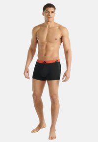 Svarta boxershorts med orange midjeresår som har en logga, gjorda av ett stretchigt material, figurnära passform, slät textur.