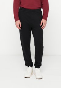 Čierne teplákové nohavice s jemnou štruktúrou, elastickým pásom a stiahnutými členkami. Nosené s bielymi teniskami a bordovou dlhým rukávom.