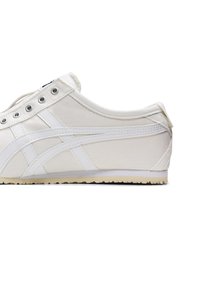 White canvas sneakers with white leather accents, round toe, flat white outsole, and six silver eyelets for laces. Minimalist design.