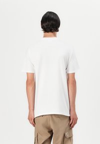 Hvit bomulls-T-skjorte med korte ermer og en avslappet passform, sett bakfra. Brukes med beige cargobukser, uten tydelige mønstre eller detaljer.