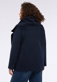 Cappotto in misto lana di colore blu navy con ampio colletto, taglio dritto, maniche lunghe e dettagli in bottone argento. Tessuto liscio con una vestibilità comoda.