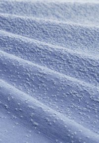 Strukturierter Stoff in Hellblau mit einem erhabenen Muster auf der Oberfläche, das eine weiche, gewebte Textur mit unterschiedlichen Tiefen zeigt.