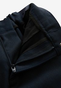 Tummansininen takki, jonka sisällä on vetoketjullinen tasku, tekstuuroitu kangas ja sileä vuori, jossa on kontrastivärinen reunus avauksessa.