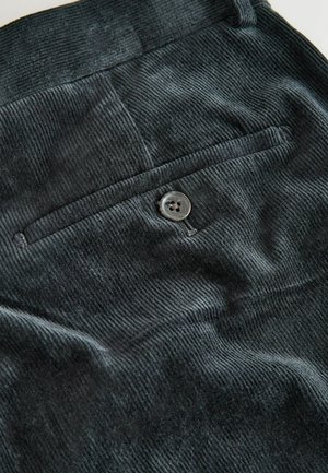 Black corduroy fabric featuring vertical ribbing, a single back pocket with a round button, and a smooth texture.