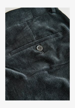 Black corduroy fabric featuring vertical ribbing, a single back pocket with a round button, and a smooth texture.