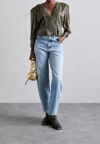 Metaalgroen, gestructureerde blouse met een V-hals en een peplum taille, gecombineerd met lichtblauwe rechte jeans en zwarte enkellaarsjes. Gouden tas in de hand.