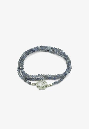 Braccialetto a più fili con perle sfaccettate grigio-blu e ciondolo a forma di fiore di loto in argento al centro su uno sfondo bianco.