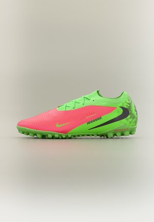 Felroze en neon groene voetbalschoen met zwarte Nike-vink en gestructureerde zool voor gebruik op kunstgras, zijaanzicht op een neutrale achtergrond.