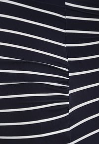 Tecido azul marinho com riscas horizontais brancas; apresenta detalhes franzidos ao longo do lado para adicionar textura. Material liso e elástico.