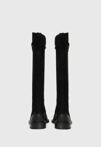 Botas altas de ante negro con una textura suave, punta redondeada y suelas de goma negra resistentes. Presentan costuras decorativas y cremalleras laterales.