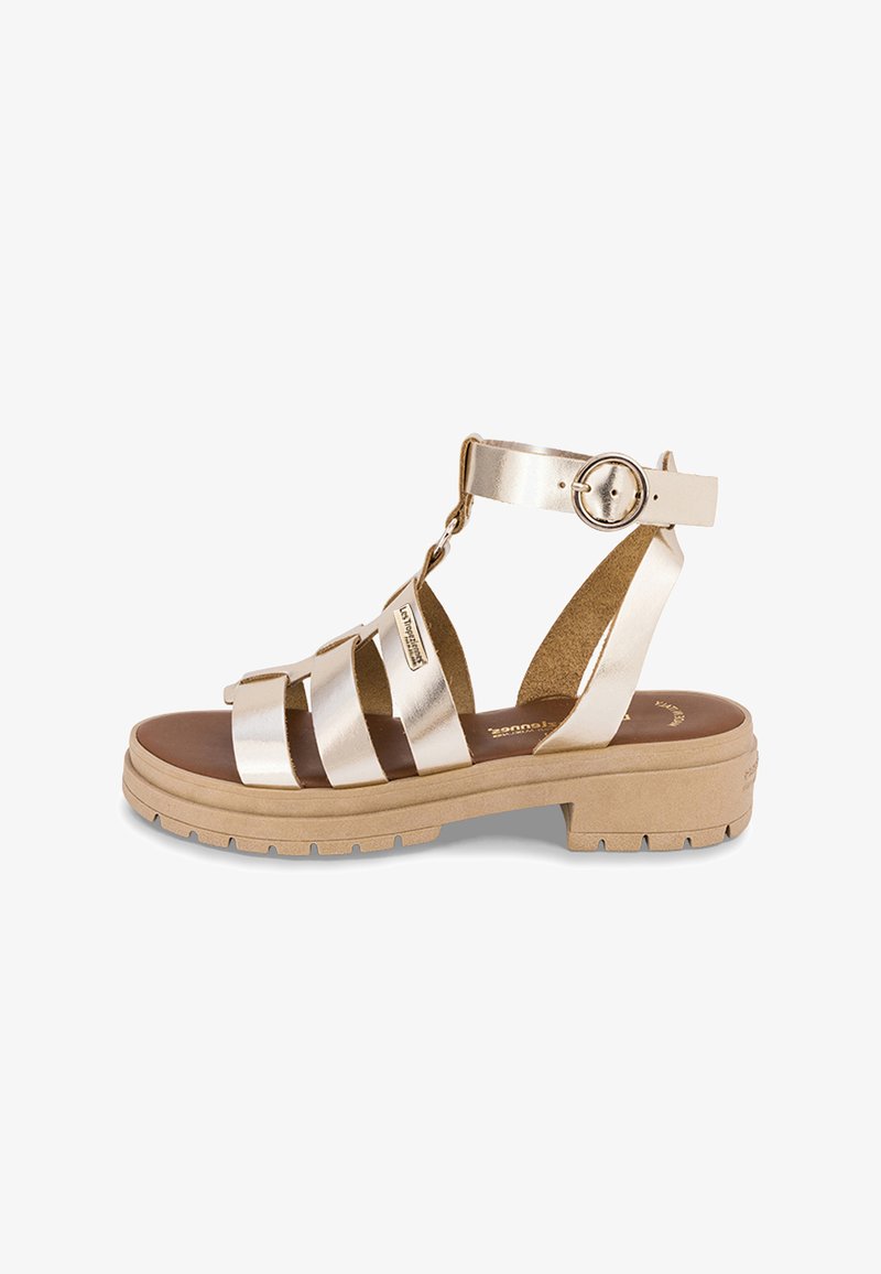 Sandali con cinturini in oro metallico con suola beige, caratterizzati da un design piatto, cinturino regolabile alla caviglia e plantare con texture.