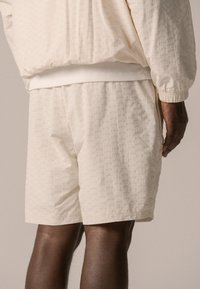 Cream-colored shorts made of textured fabric with a subtle embossed pattern. The waistband is elastic with a white trim.