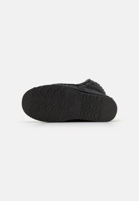 Calzature nere con suola in gomma testurizzata caratterizzata da un motivo a onda. La parte superiore è realizzata in un materiale morbido con dettagli di cucitura.