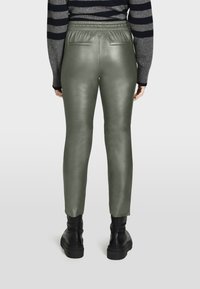 Groene, nep leren broeken met een slim fit, elastische tailleband en achterzakken. Draagt samen met zwarte, schoenen met dikke zolen.