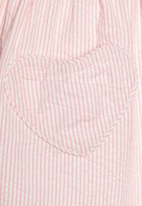 Růžová a bílá pruhovaná látka s našitou kapsou ve tvaru srdce, která má odpovídající svislé pruhy a viditelné švy.