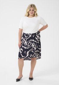 Top bianco a maniche corte abbinato a una gonna avvolgente blu navy con un motivo cremoso a vortice. Scarpe nere con fiocchi completano il look.