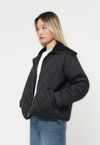 Giacca nera trapuntata con chiusura a zip, ampio colletto e tasche laterali. Caratterizzata da un materiale leggero e una vestibilità rilassata.